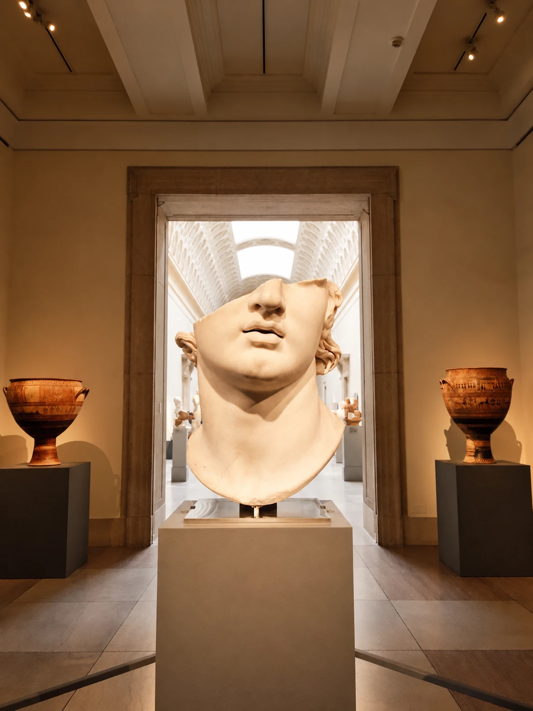 Monumental marble head displayed in a museum gallery between two ancient vases