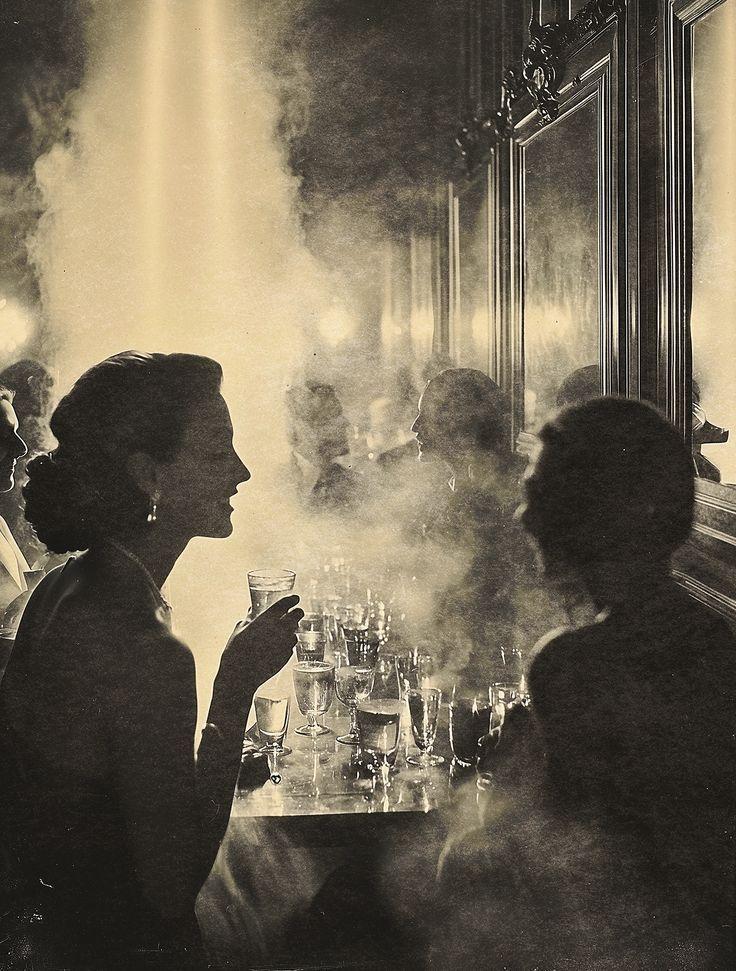 Guests talking over glasses in a softly lit, smoky salon, vintage photograph